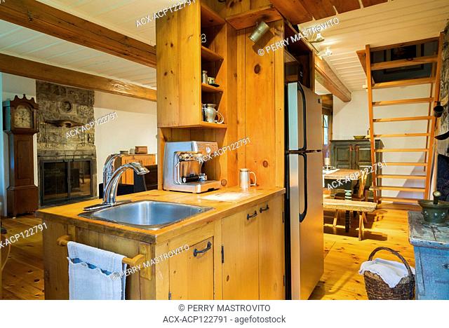Small rustic kitchen with pinewood countertop and sink cabinet, floorboards inside an old circa 1750 Canadiana style fieldstone house, Montreal, Quebec, Canada