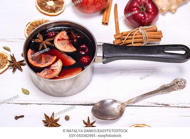 mulled wine in an aluminum ladle with a handle on a white wooden background, top view