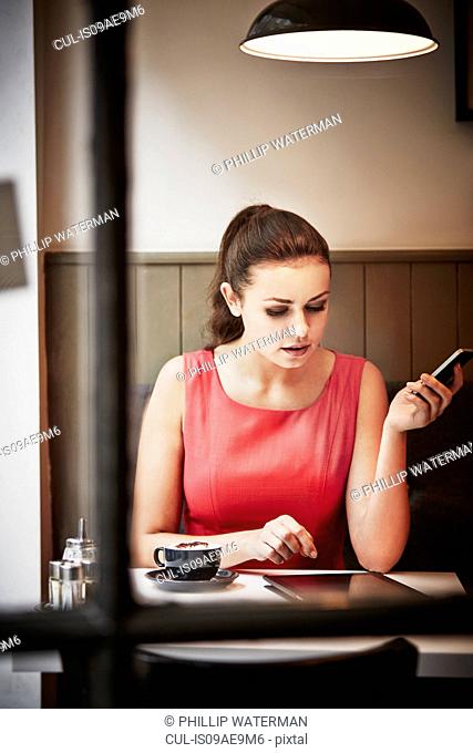 Young woman sitting in cafe with hot drink, digital tablet and smartphone