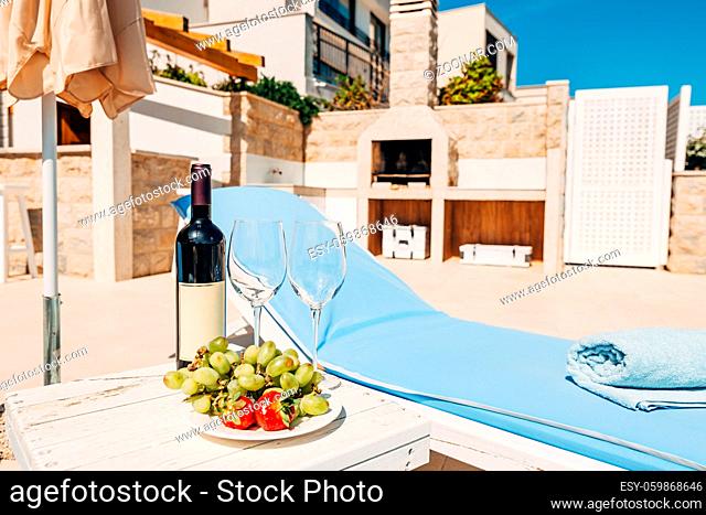 A bottle of wine, two glasses and fruit on the beach near the sunbed. In the shade of an umbrella, in the villa. High quality photo