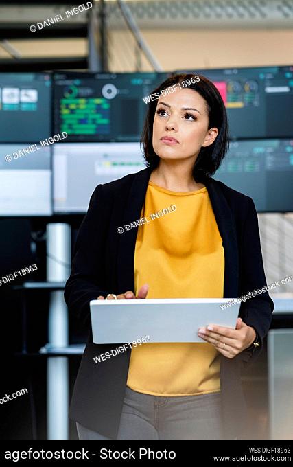 Mature businesswoman holding tablet PC in front of computer monitors