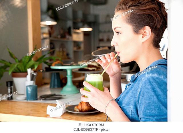 Young woman sitting at bar in cafe, drinking drink through straw