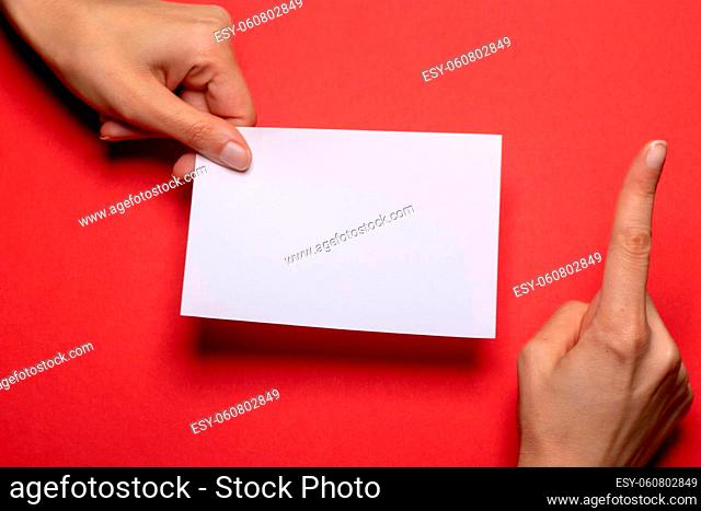 female hand holds a blank piece of paper with copy space in front of a dark red background cardboard with the hand making a warning gesture