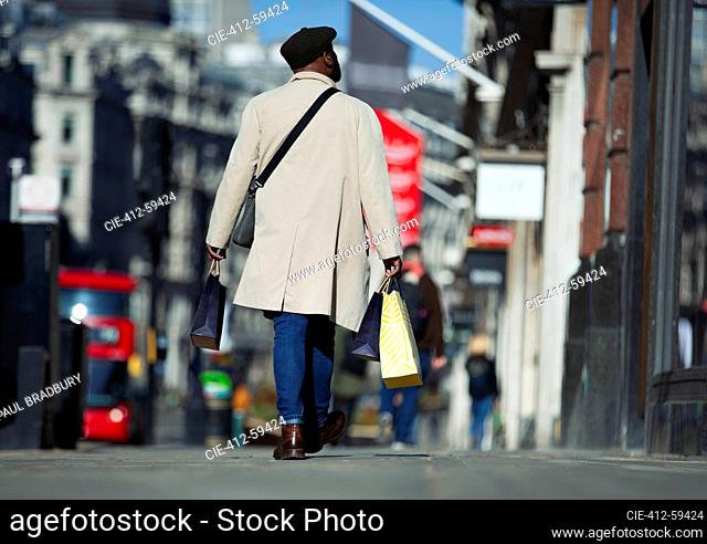 Man in trench coat carrying shopping bags on sunny city sidewalk