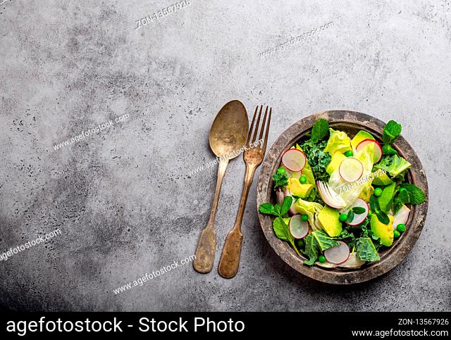 Green organic vegetables salad with avocado, kale, sprouting herbs in rustic bowl on gray concrete background, close-up, top view