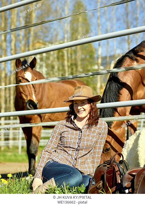 Cowgirl and saddle, horse in a paddock. South Finland in May