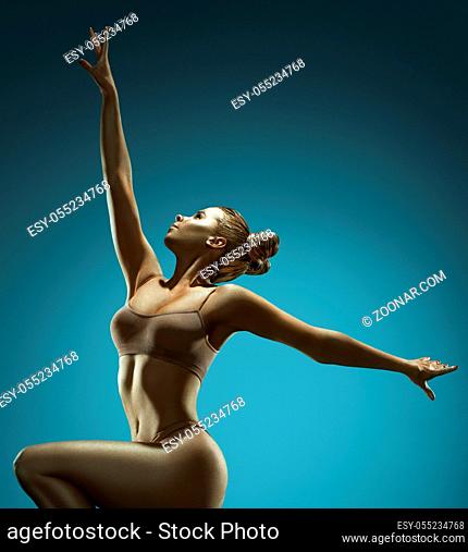 Woman with gold skin jumping gracefully in studio