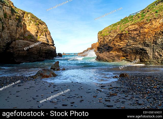 A small rock and sand beach in a sheltered cove with cliffs on the side