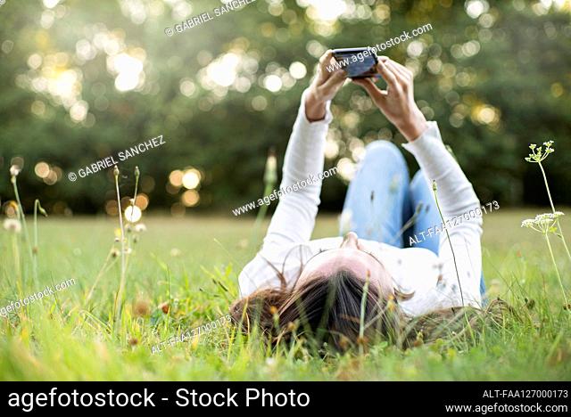 Young woman using smart phone while lying in park, Orgeval