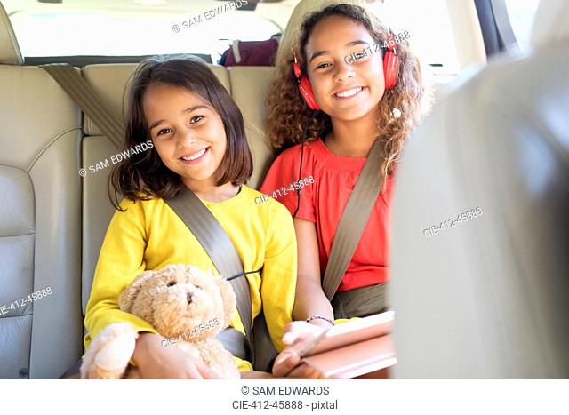 Portrait happy sisters with teddy bear riding in back seat of car