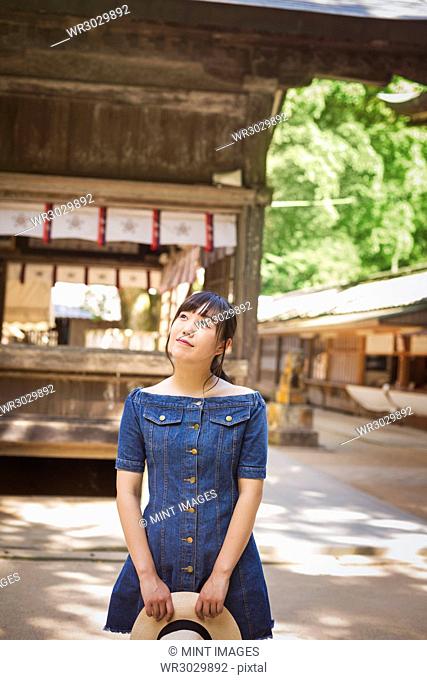 Young woman wearing blue dress and holding hat at Shinto Sakurai Shrine, Fukuoka, Japan