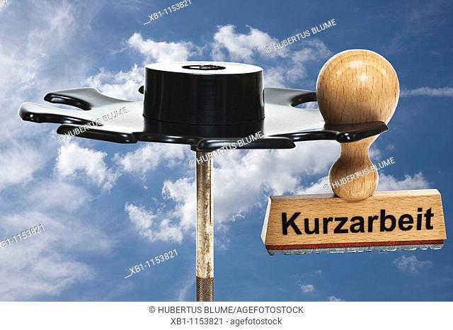 a stamp with inscription in German 'short-time work' 'Kurzarbeit' hangs in a stamp rack, in the background are sky and clouds