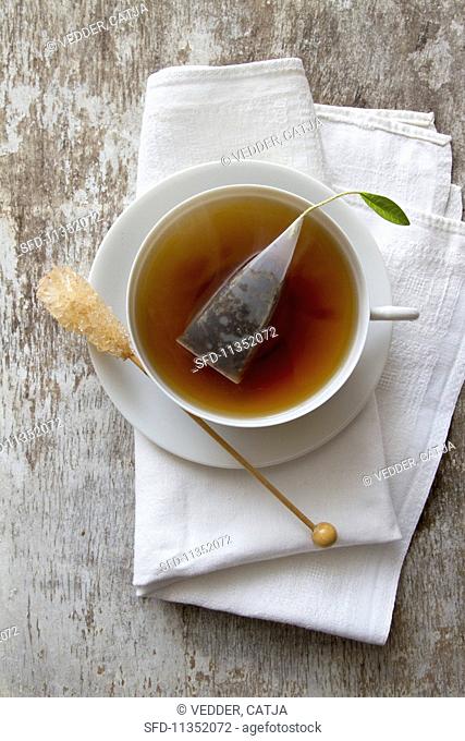 A cup of tea with a tea bag and rock candy stick on a saucer