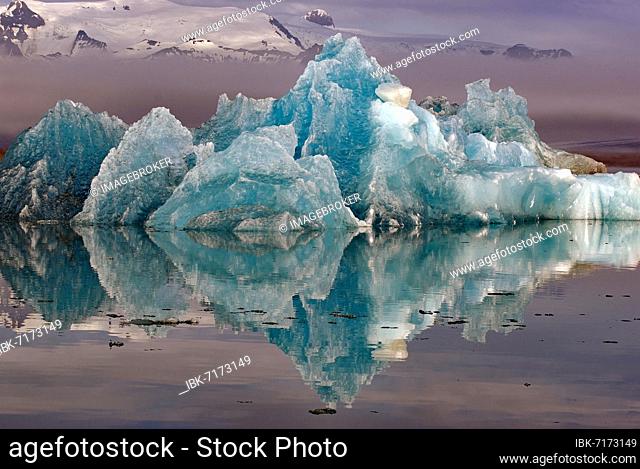 Blue iceberg reflected in the water, mountains rising out of the mist, Jökulsarlon, glacier lagoon, Scandinavia, Iceland, Europe