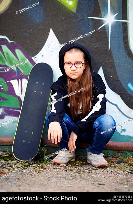 Child girl sitting near a skateboard against the wall. Vertical shot. Selective focus