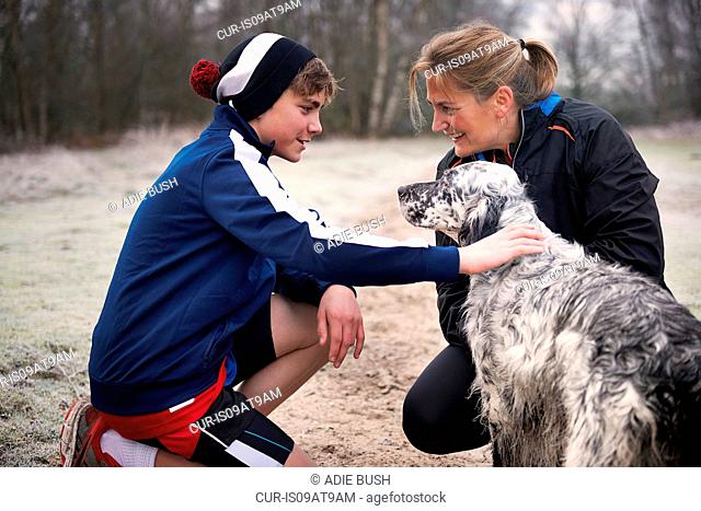 Mother and son crouching down stroking dog, face to face smiling