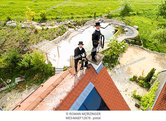 Portrait of two smiling chimney sweeps standing on house roof