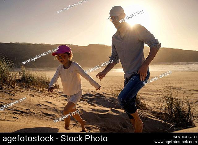 Happy father with daughter running on sand at sunset