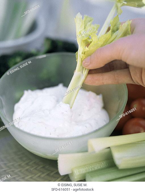 A Hand Dipping Celery Stick into Dip