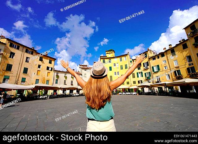 Holidays in Tuscany. Young tourist woman raising arms in the historic round square Piazza Anfiteatro in Lucca, Tuscany, Italy
