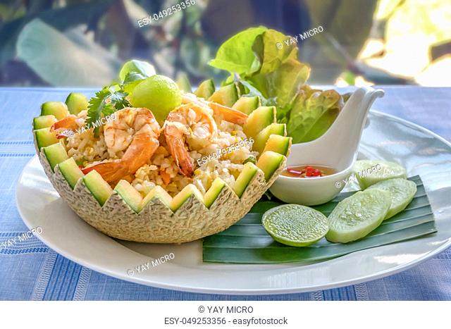 fried rice with shrimps in melon bowl served with fresh cucumber, lettuce, lime and spicy fish sauce