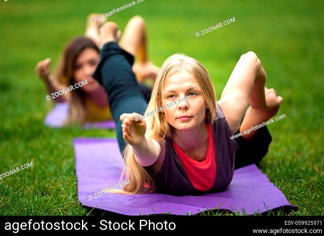 Two young women performs training for flexibility in the park, telephoto shot