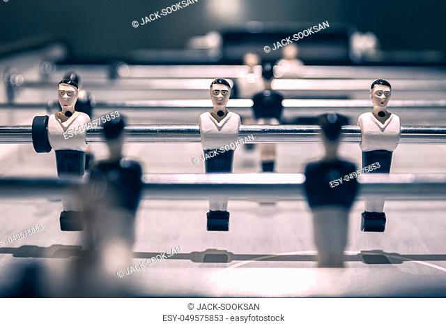 Closeup scene on player dolls in attack row rod ready before game start of vintage table football under lamp light in soft cool tone