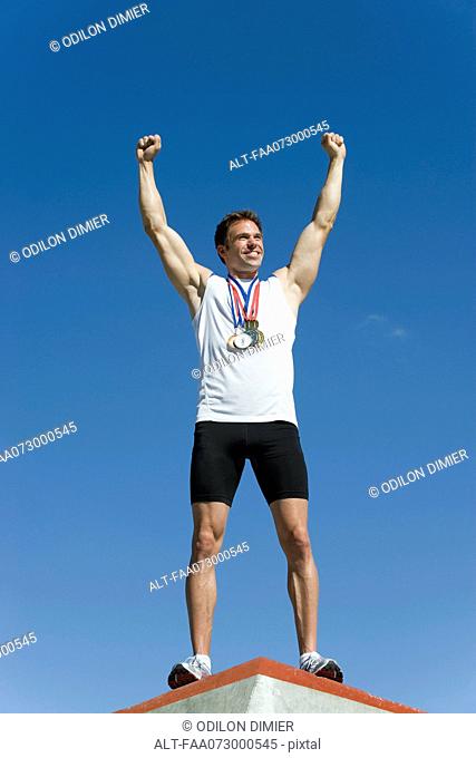 Male athlete standing on winner's podium with arms raised in victory