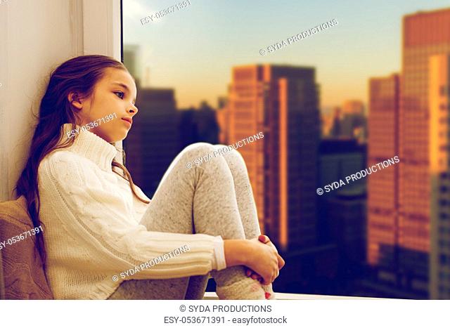 sad girl sitting on sill at home window over city