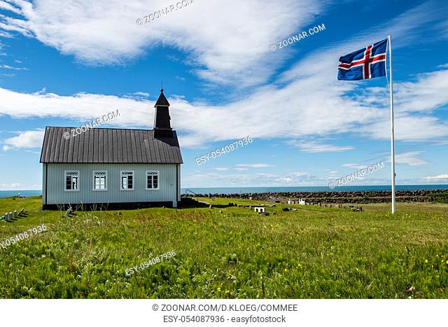 Strandkirkja on Iceland with Icelandic flag, green meadow and ocean