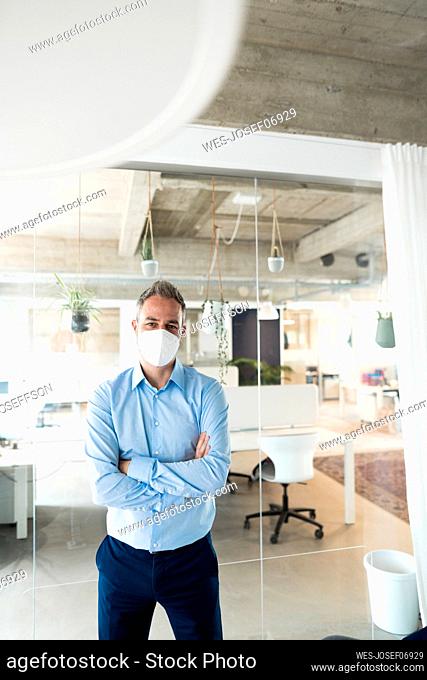 Businessman with arms crossed wearing protective face mask in office