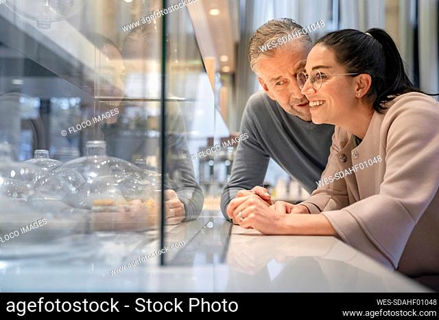 Smiling businesswoman looking at cake display while standing by man at modern cafe