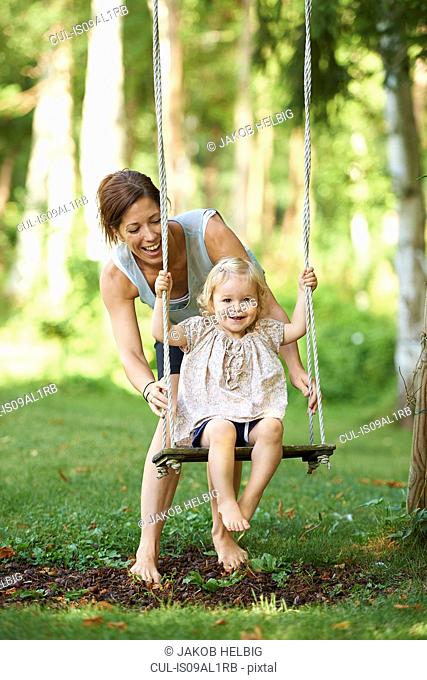 Mid adult mother pushing toddler daughter on garden swing
