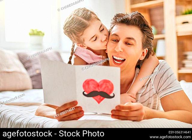 Happy father's day! Child daughter congratulates dad and gives him postcard. Daddy and girl smiling and hugging. Family holiday and togetherness