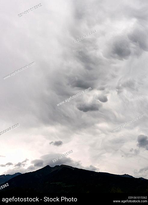 abstract unusual cloudy sky background in milky gray and white and a dark mountain silhouette