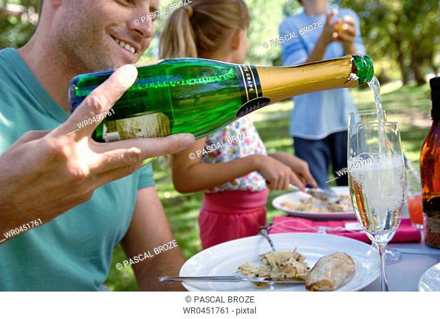 Side profile of a mid adult man with their two children in a park and pouring champagne