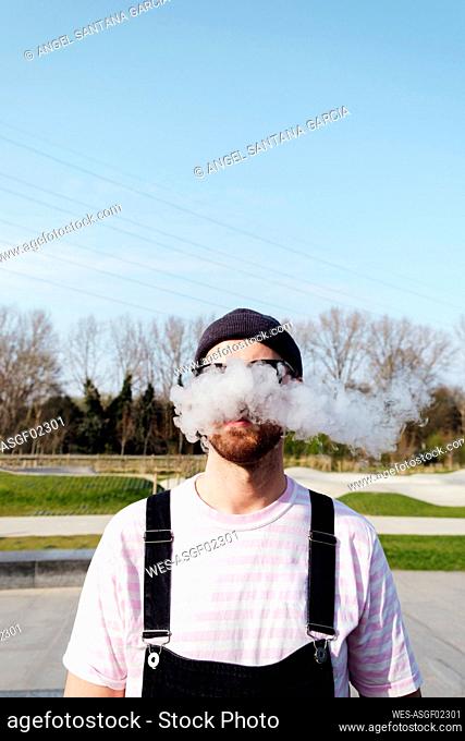 Man exhaling smoke standing on sunny day