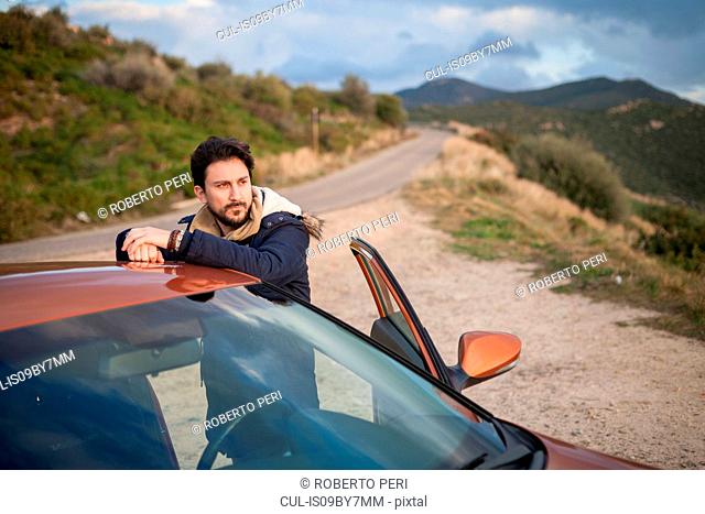 Man resting against car on roadside, enjoying view on hilltop, Villasimius, Sardegna, Italy