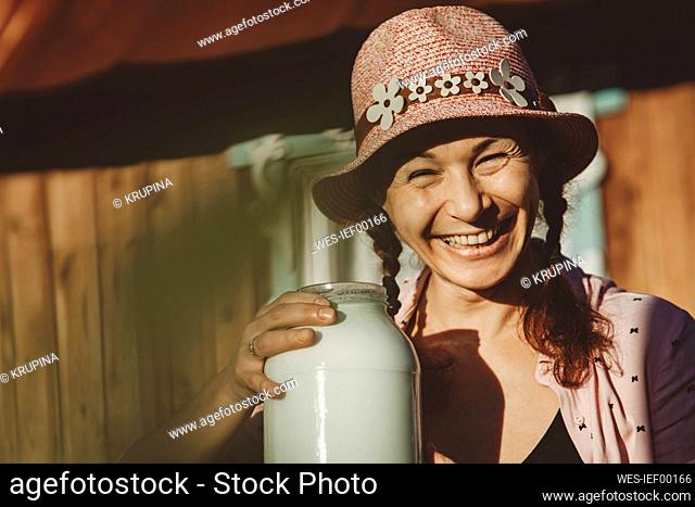 Cheerful woman wearing bucket hat with jar of milk on sunny day