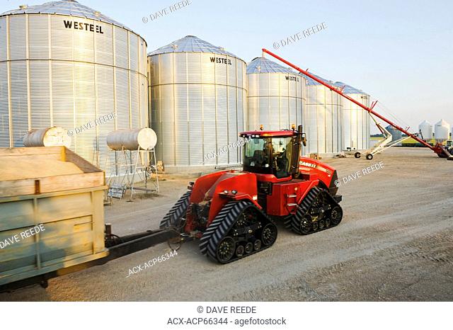 a tractor and grain wagon loaded with wheat passes grain storage bins during the harvest, near Lorette, Manitoba, Canada