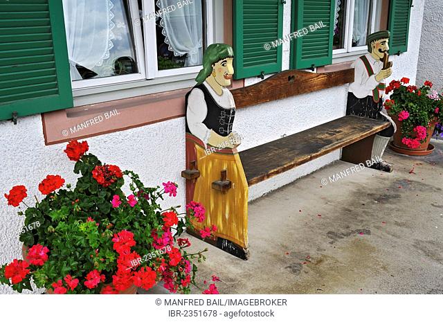 Bench with wooden figures and Geraniums (Pelargonium), Fruehlingstrasse, Garmisch-Partenkirchen, Bavaria, Germany, Europe