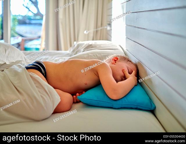 Three year old toddler boy sleeping on blue pillow under blanket