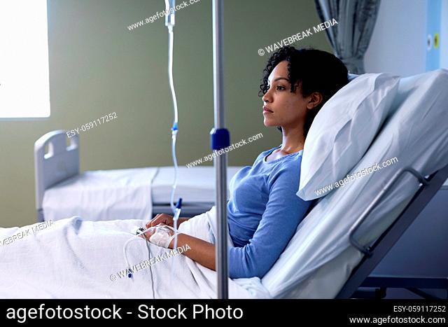 Mixed race female patient sitting in hospital bed wearing fingertip pulse oximeter and iv drip