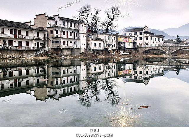 Mirror image of traditional houses and bare trees by lake, Lucun Village, Anhui Province, China