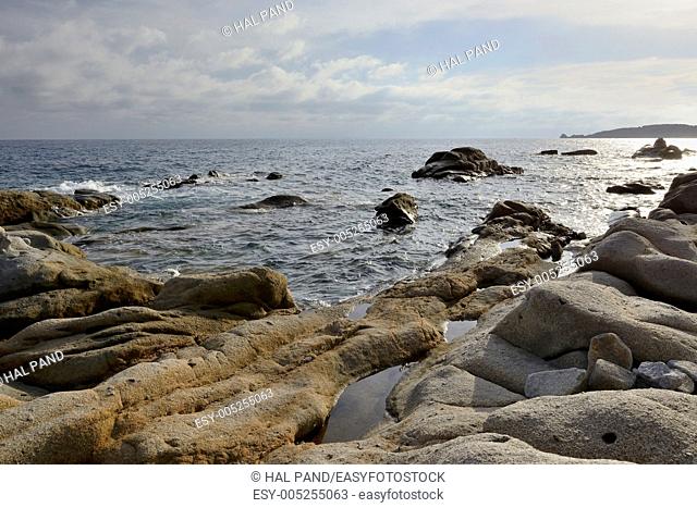 landscape of the southern coast of the green island in mediterranean sea, in foreground clear water and rocks lighted by sunset light