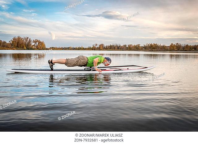 senior male doing pushups and planks for warming up on a paddleboard before paddling workout on a lake in Colorado