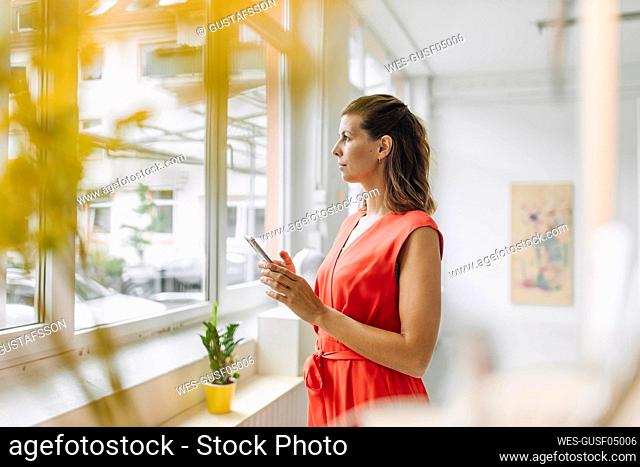 Businesswoman holding digital tablet and looking through window in office