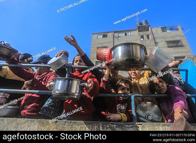 19 December 2023, Palestinian Territories, Rafah: Palestinians gather with pots to receive food at a donation point provided by a charitable organization in...