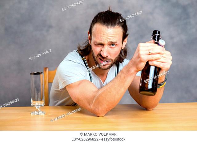 young man in front of gray background opening a beer bottle