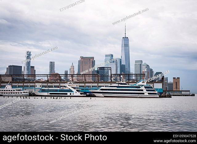 Manhattan skyline with yachts moored at the pier from the greenway of the Hudson River in New York by an overcast blue sky